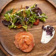 Gebeizter Lachs als Vorspeise, serviert mit einem frischen Salat und cremiger Sauce auf einem Holzbrett.