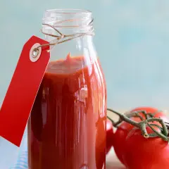 Glasflasche mit selbstgemachtem Tomatenketchup, rotem Anhänger und frischen Tomaten.