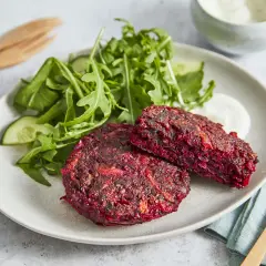 Zwei herzhafte rote Bete Bratlinge auf einem Teller mit Salat und Dip.