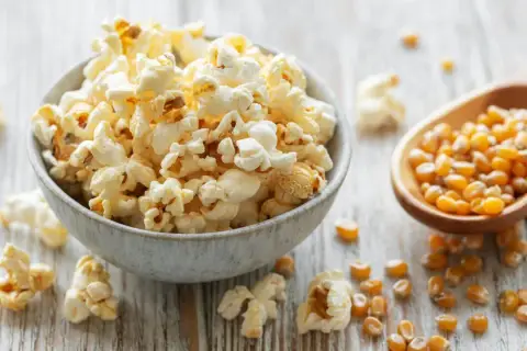 Frisch zubereiteter popcorn im topf, dane Maiskörner auf einem Holzlöffel.