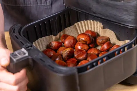 Maronen im Airfryer, bereit für die Zubereitung. Die braunen, glänzenden Früchte liegen auf Backpapier in dem schwarzen Korb.