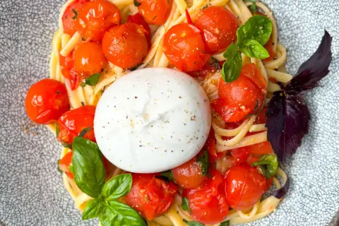 Ein cremiger Burrata Salat mit Pasta, Kirschtomaten und Basilikum auf einem gemusterten Teller.
