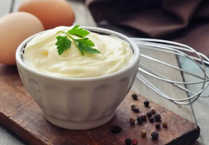 Frische Eier und Petersilie auf einem Holzbrett, bereit, um köstliche Mayonnaise selber machen. Ein Schneebesen liegt daneben.