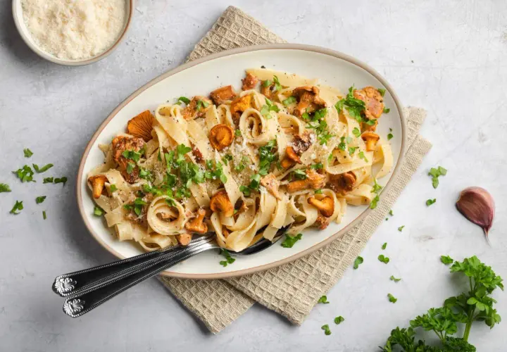 Tagliatelle mit Pfifferlingen, garniert mit Petersilie und Parmesan. Ein köstliches Herbstgericht, das die Aromen der Natur einfängt.