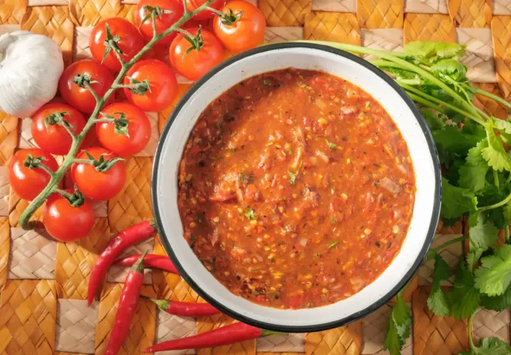 Schüssel mit würziger Salsa Brava, daneben frische Tomaten, Knoblauch und Chilischoten. Perfekt für Ihr nächstes salsa brava rezept!