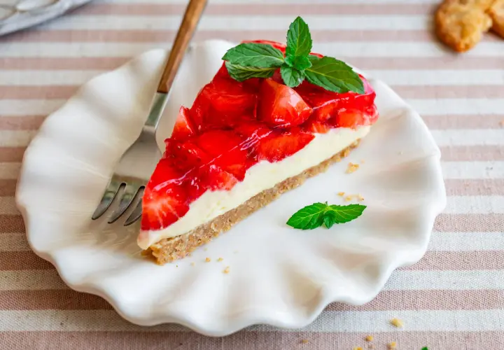 Ein Stück Erdbeerkuchen mit Frischkäsefüllung und glasierten Erdbeeren, garniert mit Minze. Perfekt für einfache Desserts ohne Backen.