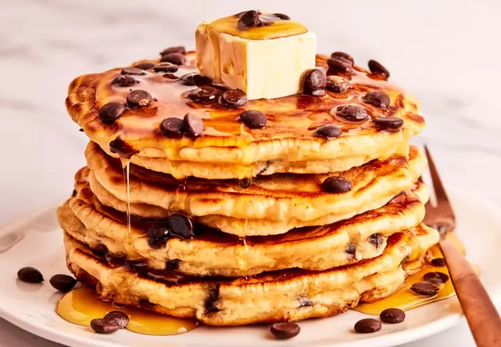 Ein Stapel saftiger Schokoladensplitter-Pfannkuchen, übergossen mit Ahornsirup und einem Stück Butter.