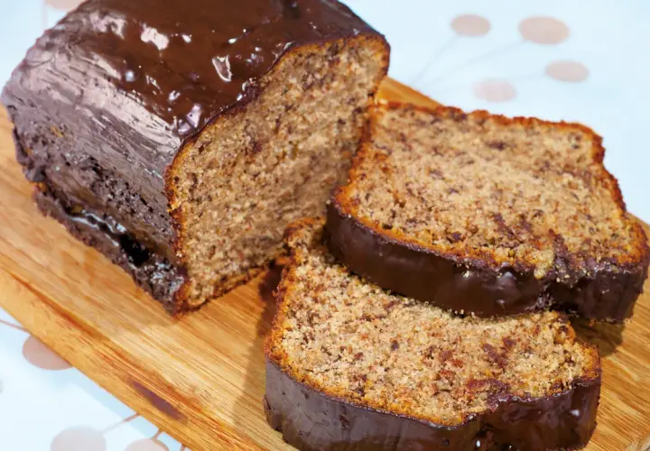 Ein **super saftiger Bananenkuchen** mit Schokoladenglasur, angeschnitten auf einem Holzbrett.