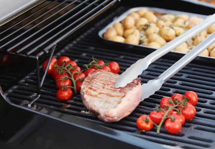 Duroc secreto zubereitung: Ein saftiges Steak wird mit Kirschtomaten auf dem Grill zubereitet. Daneben liegen Kartoffeln in einer Schale.