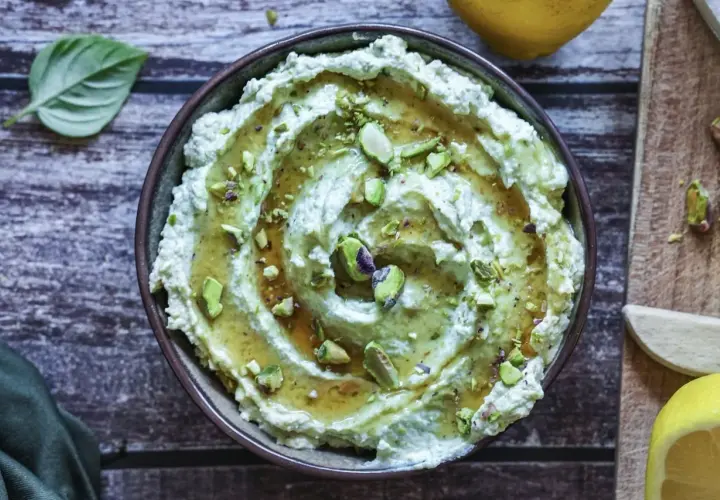 Cremiges Avocado Basilikum Pesto mit Pistazien und Honig beträufelt, garniert mit frischen Basilikumblättern und Zitronenspalten.