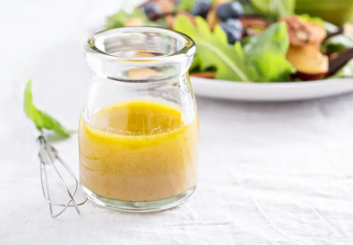 Ein Glas mit gelber Vinaigrette, daneben ein Schneebesen. Ein einfaches vinaigrette rezept für frische Salate.