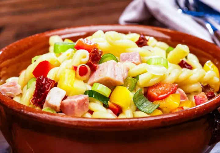 Leckerer nudelsalat ohne mayonnaise mit bunten Paprikawürfeln, Schinken und Frühlingszwiebeln in einer Tonschüssel.