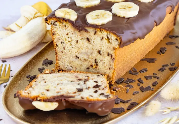 Saftiger Bananen Buttermilch Kuchen mit Schokoladenglasur und Bananenscheiben, garniert mit Schokostückchen.