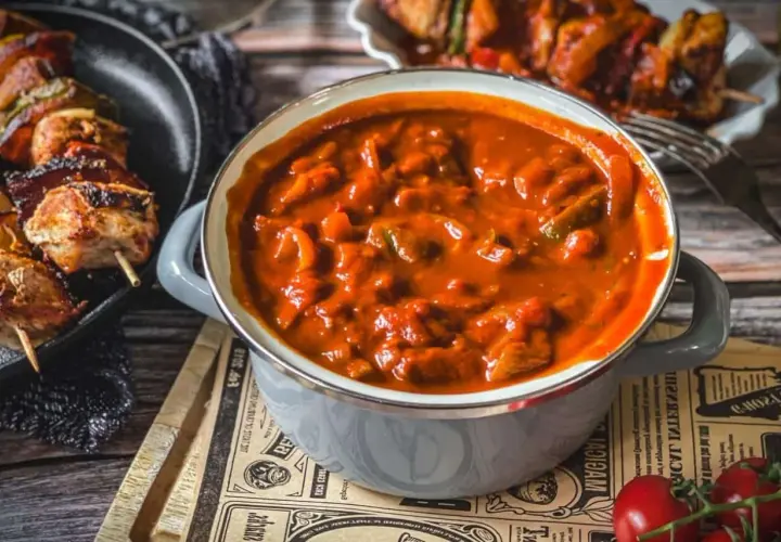 Herzhafte schaschlik sauce wie im imbiss, mit Fleischstücken und Paprika, dane daneben gegrillte Spieße.