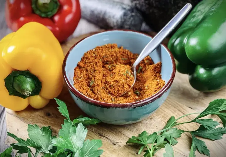 Schüssel mit Gewürzmischung, perfekt zum pul biber selbst mischen. Bunte Paprika und frische Petersilie liegen daneben.