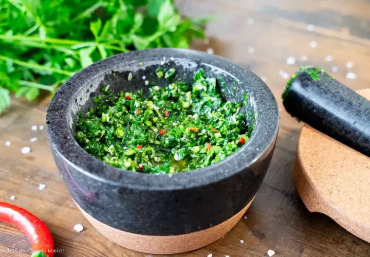 Frisches Chimichurri-Rezept im Mörser, bereit zum Verfeinern von Grillgut. Kräuter, Chili und Öl duften verführerisch.