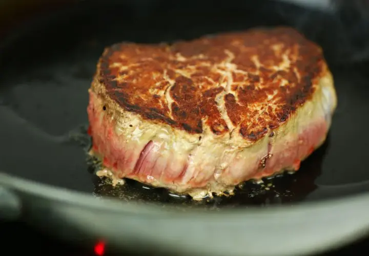 Ein saftiges Steak brät in einer Pfanne. Die Kruste ist goldbraun, das Innere noch rosa. Perfekt, um ein Steak richtig braten zu lernen.