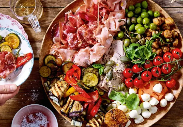 Vielfältige Antipasti Platte Ideen: Wurst, Käse, Oliven, gegrilltes Gemüse und frische Tomaten auf rustikalem Holzbrett.