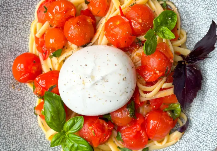 Ein cremiger Burrata Salat mit Pasta, Kirschtomaten und Basilikum auf einem gemusterten Teller.