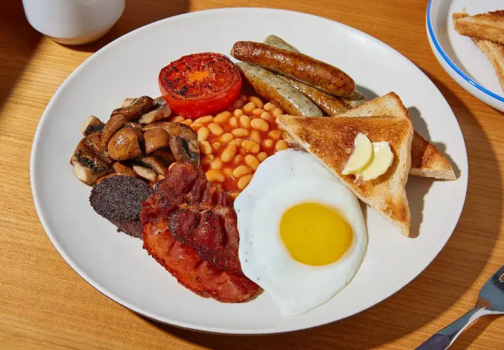 Ein üppiges **full English breakfast** mit Spiegelei, Speck, Würstchen, Bohnen, Pilzen, Tomate, Blutwurst und Toast.