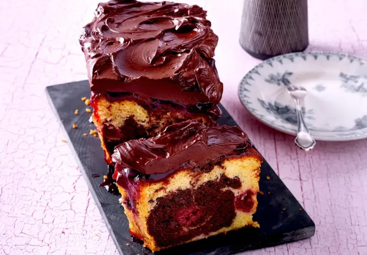Saftiger Marmorkuchen mit Kirschen und dunkler Schokoladenglasur, auf einem schwarzen Brett serviert.