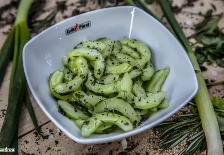 Frischer gurkensalat mit dill, garniert mit Pfeffer und Kräutern, serviert in einer weißen Schüssel.