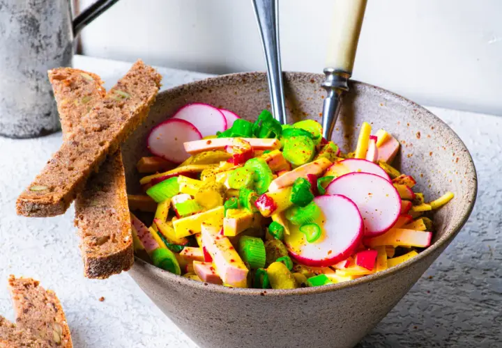 Schmackhafter Schweizer Wurstsalat mit Radieschen und Lauchzwiebeln, serviert mit Vollkornbrot. Ein tolles Rezept für den Sommer!