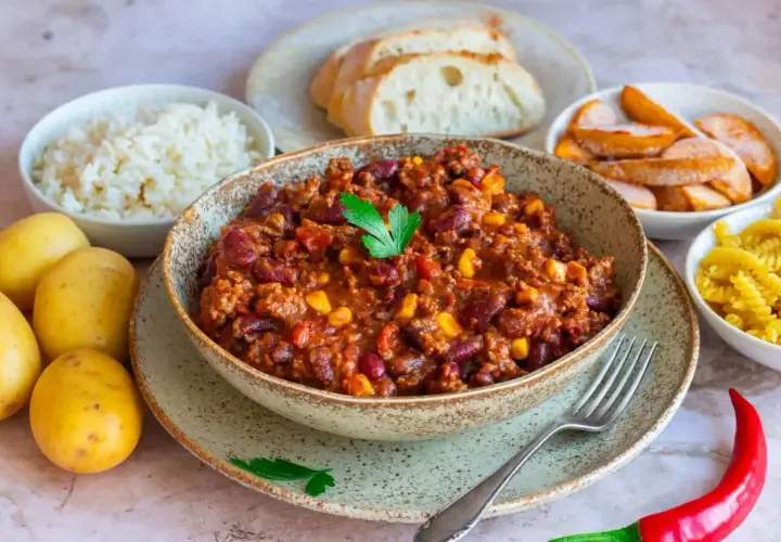 Herzhaftes Chili con Carne als Beilage, serviert mit Reis, Brot, Kartoffeln und Nudeln. Ein Festmahl!