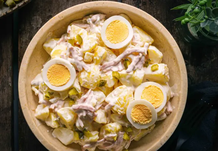 Schüssel mit Kartoffelsalat und Fleischsalat, garniert mit hartgekochten Eiern und Gewürzgurken.