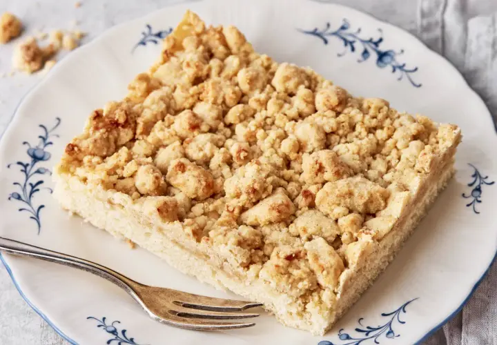 Ein Stück Streuselkuchen, wie von Oma nach DDR-Rezept, mit knusprigen Streuseln auf einem Teller mit blauem Rand.