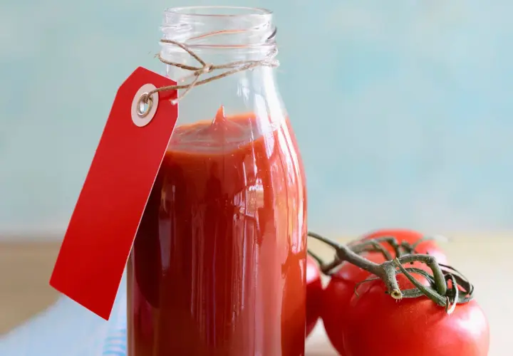 Glasflasche mit selbstgemachtem Tomatenketchup, rotem Anhänger und frischen Tomaten.