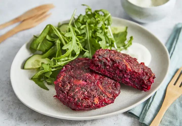 Zwei herzhafte rote Bete Bratlinge auf einem Teller mit Salat und Dip.