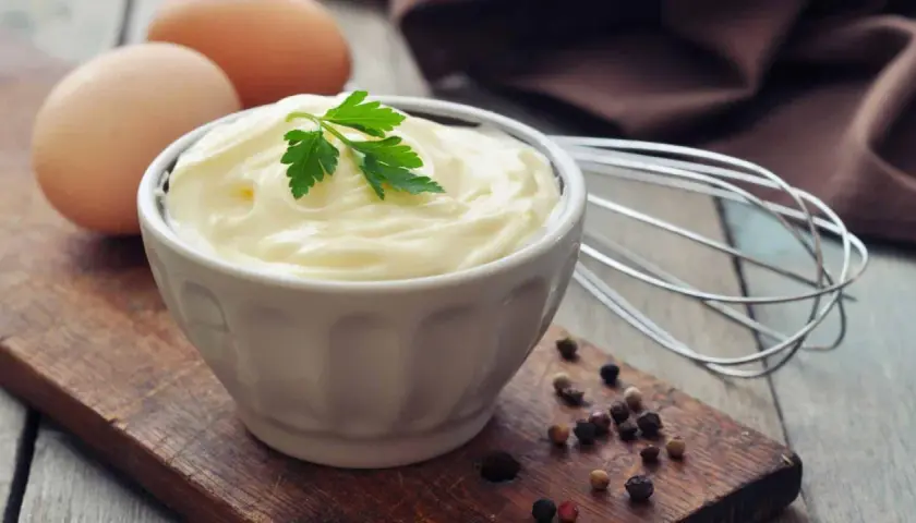 Frische Eier und Petersilie auf einem Holzbrett, bereit, um köstliche Mayonnaise selber machen. Ein Schneebesen liegt daneben.