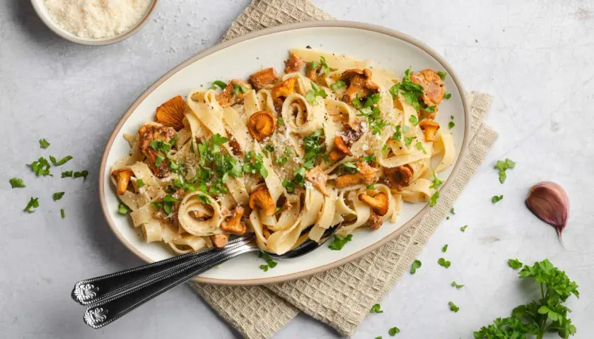 Tagliatelle mit Pfifferlingen, garniert mit Petersilie und Parmesan. Ein köstliches Herbstgericht, das die Aromen der Natur einfängt.