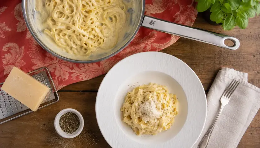 Cremige Pasta Alfredo, zubereitet nach einem einfachen Rezept. Serviert auf einem Teller mit frisch geriebenem Parmesan und Pfeffer.
