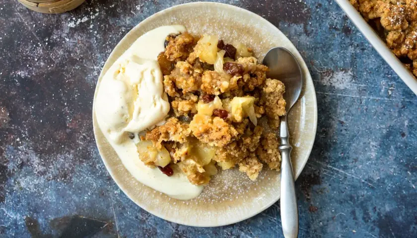 Ein Teller mit warmem Apfelcrumble und einer Kugel cremigem Vanilleeis, bestäubt mit Puderzucker.