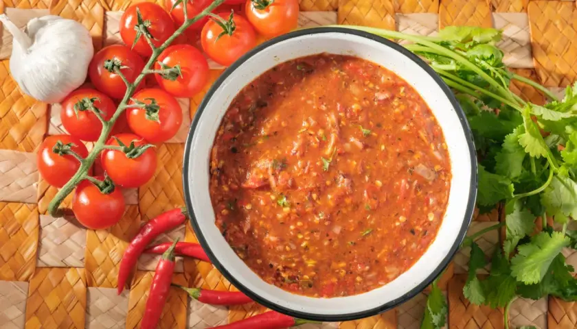 Schüssel mit würziger Salsa Brava, daneben frische Tomaten, Knoblauch und Chilischoten. Perfekt für Ihr nächstes salsa brava rezept!