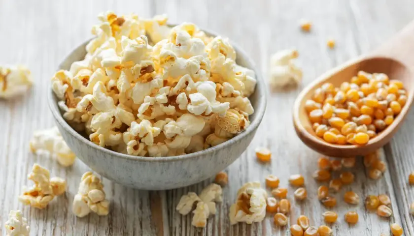 Frisch zubereiteter popcorn im topf, dane Maiskörner auf einem Holzlöffel.