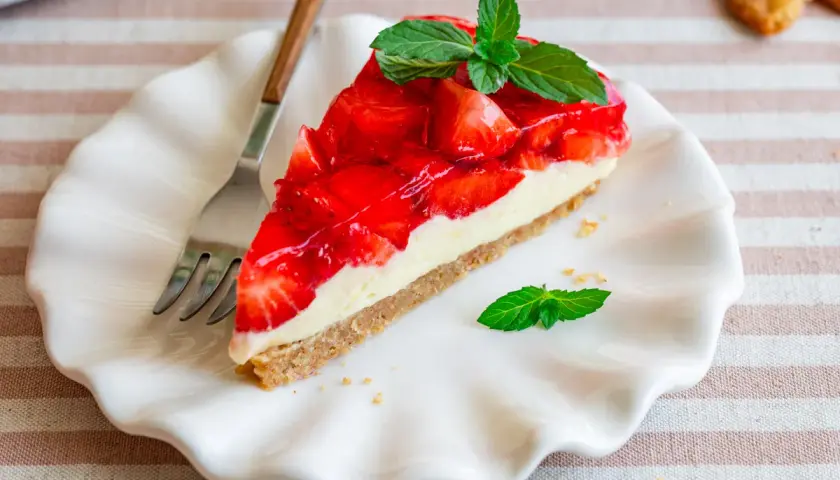 Ein Stück Erdbeerkuchen mit Frischkäsefüllung und glasierten Erdbeeren, garniert mit Minze. Perfekt für einfache Desserts ohne Backen.