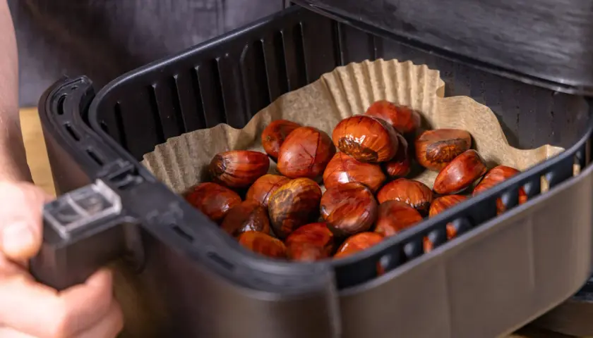 Maronen im Airfryer, bereit für die Zubereitung. Die braunen, glänzenden Früchte liegen auf Backpapier in dem schwarzen Korb.