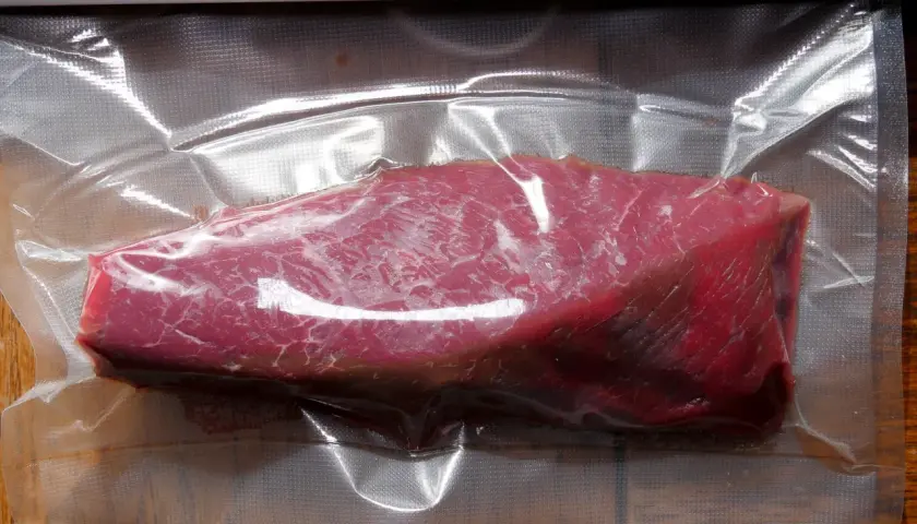 Ein roher Kalbstafelspitz, vakuumiert für Sous-Vide-Garen, liegt auf einem Holztisch.