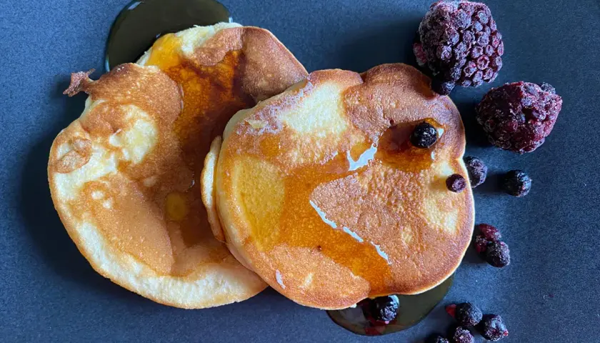 Goldbraune Pfannkuchen ohne Backpulver, beträufelt mit Sirup und garniert mit gefrorenen Beeren. Ein Genuss!