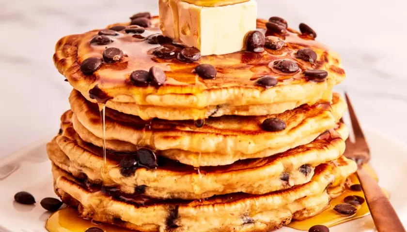 Ein Stapel saftiger Schokoladensplitter-Pfannkuchen, übergossen mit Ahornsirup und einem Stück Butter.