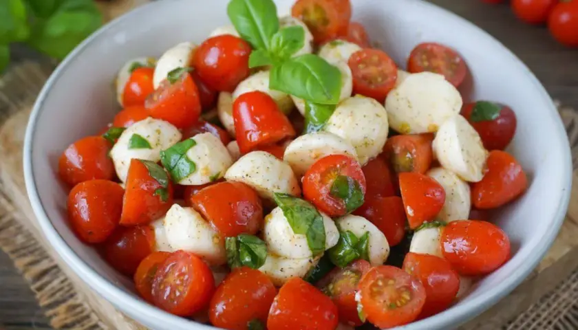 Ein frischer italienischer Salat mit Kirschtomaten, Mozzarella-Bällchen und Basilikumblättern, appetitlich in einer Schüssel angerichtet.