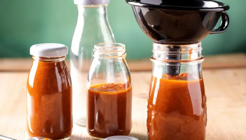 Selbstgemachter Ketchup wird in Gläser abgefüllt. Ein Trichter hilft beim Abfüllen für die Konservierung.