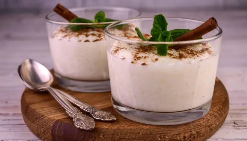 Zwei Gläser cremiger Milchreis, garniert mit Zimt und Minze. Ein einfaches Milchreis Rezept, das süße Erinnerungen weckt.