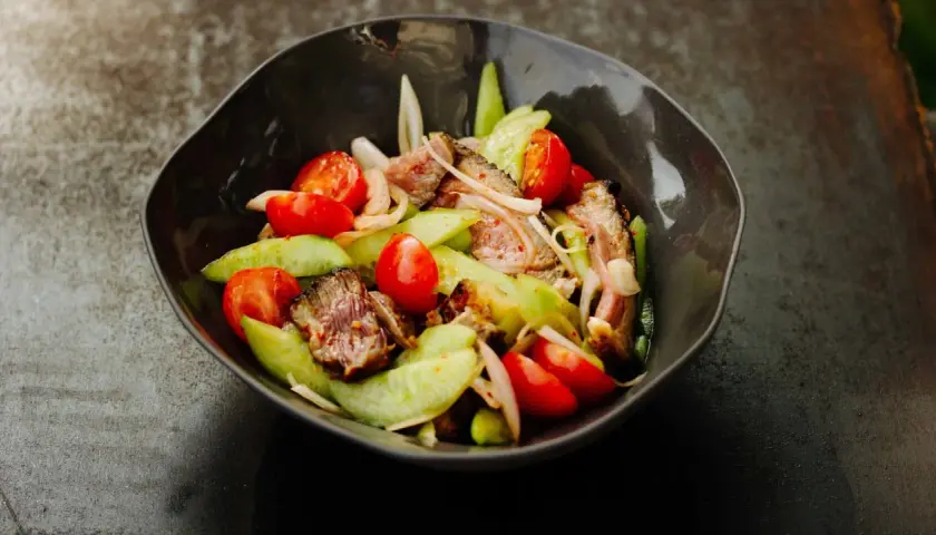 Ein herzhafter Yam Nua Salat mit gegrilltem Rindfleisch, Tomaten und Gurken in einer dunklen Schüssel.