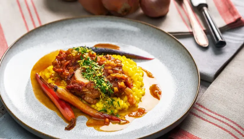Ein köstliches Ossobuco Rezept mit zartem Kalbfleisch, serviert auf cremigem Safranrisotto und garniert mit frischen Kräutern und karamellisierten Karotten.
