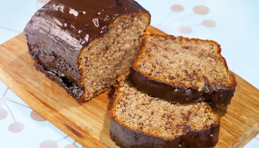 Ein **super saftiger Bananenkuchen** mit Schokoladenglasur, angeschnitten auf einem Holzbrett.