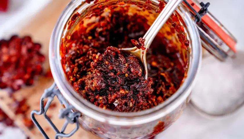Ein Glas mit selbstgemachtem, würzigem Chiliöl. Ein Löffel hebt die glänzende, rote Masse hervor, perfekt für jedes crispy chili oil rezept.